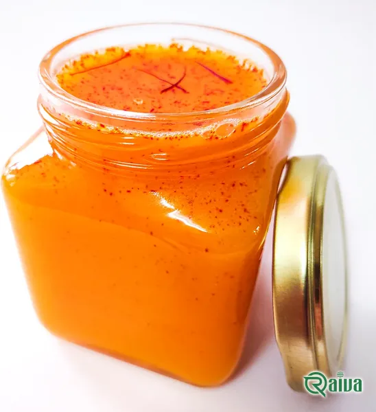 An open glass jar of orange saffron honey flecked with saffron, its lid beside it (view 1)